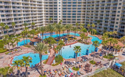 Discover a sprawling tropical resort pool complex surrounded by palm trees, sun loungers, and high-rise vacation rental accommodations.