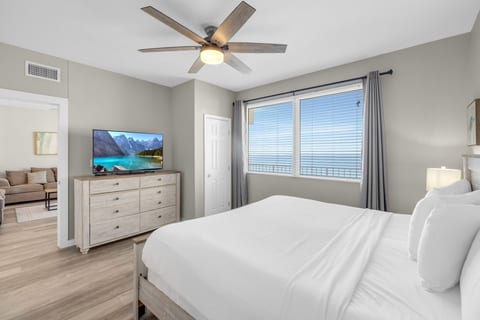 Spacious king bedroom includes a dresser with TV, large windows that bring in abundant natural light, and a ceiling fan for added comfort.