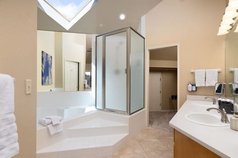 Bright spa-like bath with soaking tub, skylight, and dual sinks