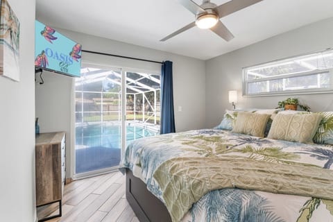 Primary bedroom — king bed with coastal luxury bedding, wall-mounted smart TV, and direct sliding glass door access to the private screened pool.