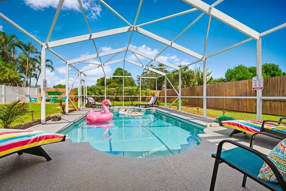 Screened-in private pool at Sun Oasis, a vacation rental in St. Petersburg, FL — crystal-clear water, lounge chairs, and lush tropical landscaping in a fully fenced backyard.