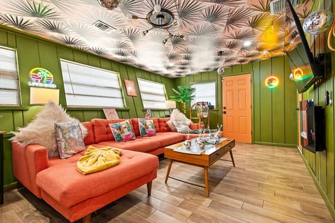The Disco Lounge at Tropical Disco — retro-inspired gathering space with coral sectional, palm-print ceiling, multiple disco balls, and neon signs. St. Pete, FL.