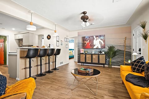 Open-plan living and kitchen — 65-inch smart TV, breakfast bar with 4 stools, and mustard yellow sofas. 4-bedroom vacation rental, St. Petersburg, FL.