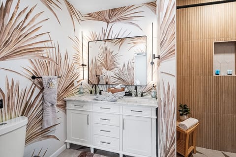 Spa-like ensuite — dual marble vanity, backlit mirror, palm-leaf mural walls, and oversized walk-in rain shower. St. Pete, FL pool home.