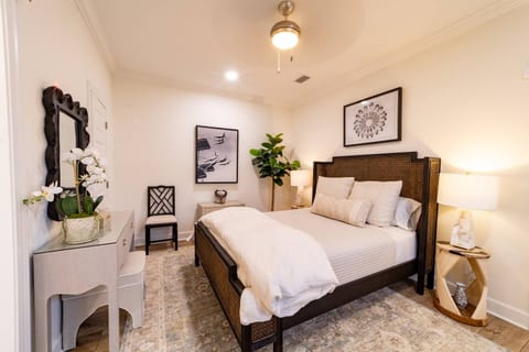 Relax in a serene, thoughtfully designed bedroom featuring a plush bed with soft, hotel-quality linens, warm lighting, and a clean, elegant aesthetic. A cozy vanity space, curated artwork, and subtle greenery add comfort, style, and a peaceful feel.
