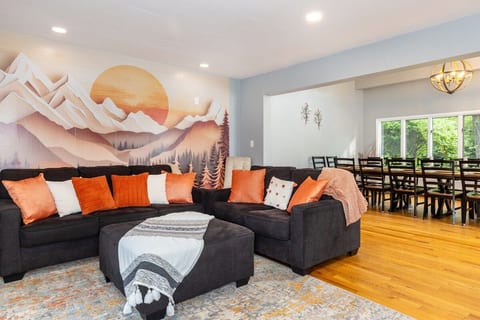 Spacious open-concept living room with a huge sectional, custom mountain mural, and dining for 20+ guests. ⭐