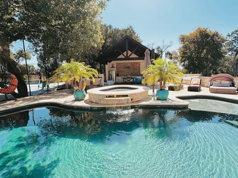 Custom over-sized (36,000 gallon) pool featuring an elevated spa w/a waterfall spillover, lush tropical plants, & covered outdoor kitchen complete w/full size outdoor bathroom w/shower.