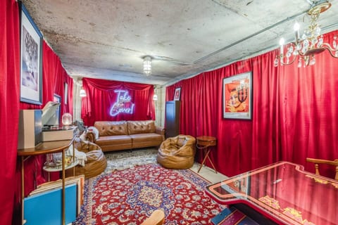 Very unique 1960's bomb shelter turned speakeasy, featuring bold red curtains, a leather couch, arcade game table, and vintage decor — perfect for a fun and memorable hangout!