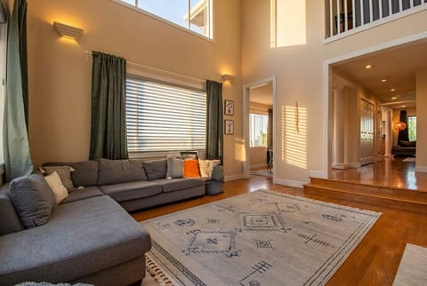Sunny, double-height lounge with plush sectional and hardwood floors