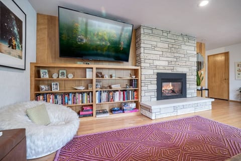Cozy reading nook by the fireplace, complete with a plush chair, a stocked bookshelf, and a large TV for ultimate relaxation!