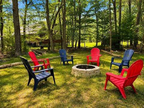 Firepit in the woods with six Adirondack chairs.
