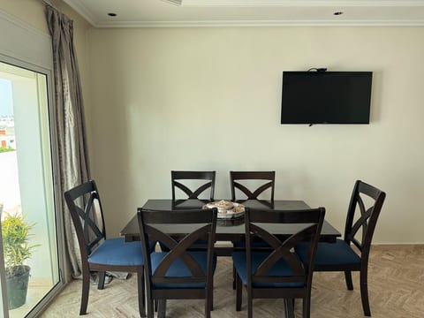 Elegant dining area with a 6-seat dark wood table, matching blue upholstered chairs, large flat-screen TV, and herringbone floor — ideal for family meals or group gatherings.