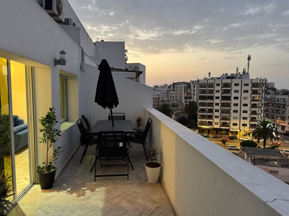 Private rooftop terrace with full outdoor dining set, parasol and breathtaking panoramic views over the Casablanca skyline at golden hour — the perfect spot for sunset dinners above the city.