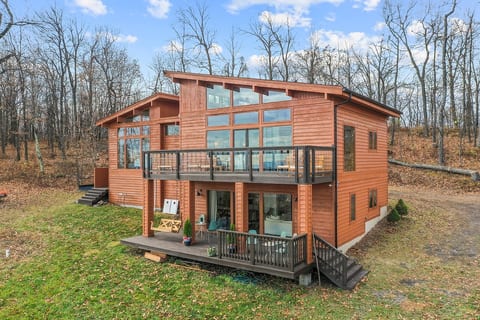 Birds eye view of retreat showing floor to ceiling windows, two balconies, porch swing, outdoor shower, outdoor patio seating, outdoor games in the nature