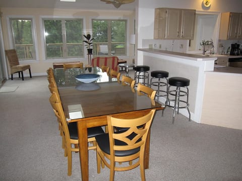 View of the dining table which has 10 chairs and extra seating can be accommodated using the benches in the sunroom. Three bar stools on the right face the kitchen. Open floor plan.