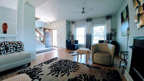 View of 2/3 of the living room from the middle seating area near the fireplace. Front door and stairs to the second level also. Lots of light and windows in an open floor plan.