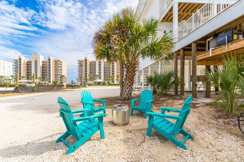 Coastal fire pit lounge with teal chairs, steps from the beach.