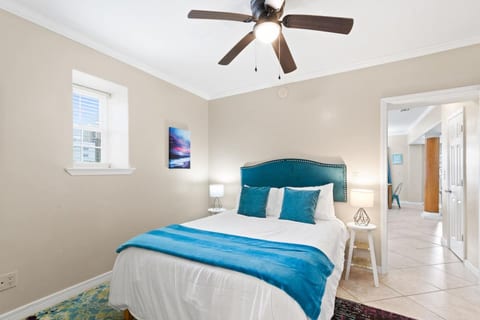 Sunny bedroom with queen bed, teal accents, ceiling fan, and lamps.
