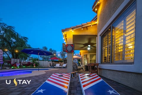 Twilight pool patio with string lights, cornhole, and lounge space