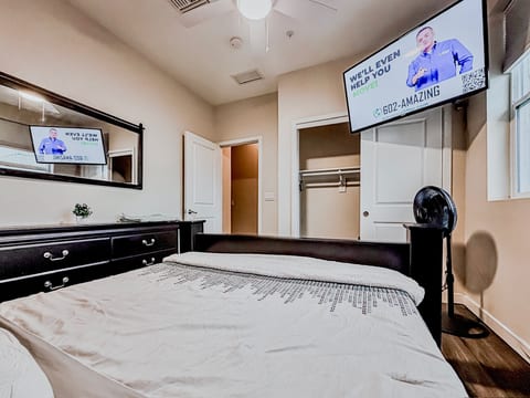 Bright bedroom with wall-mounted TV, dresser, open closet & ceiling fan.