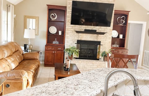 Comfortable living room with fireplace, large TV, and open connection to the kitchen.