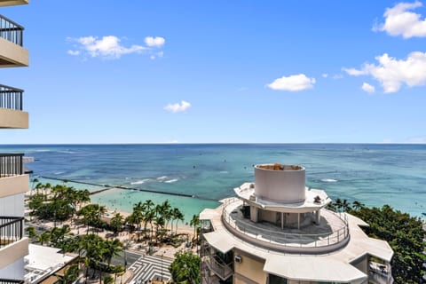 From the lanai, the beach curves out below with surfers riding the break offshore.