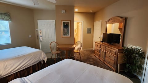 Spacious bedroom featuring two beds, dresser storage, TV, and a small table with seating.