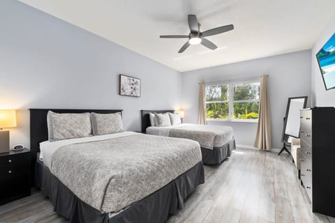 Spacious bedroom featuring two comfortable beds, ceiling fan, TV, dresser storage, and bright natural light.