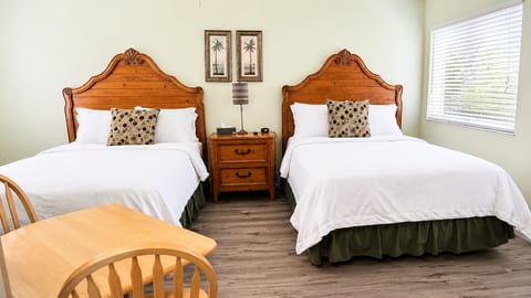 Bright bedroom with two comfortable beds, wood-look flooring, bedside lighting, and plenty of natural light.