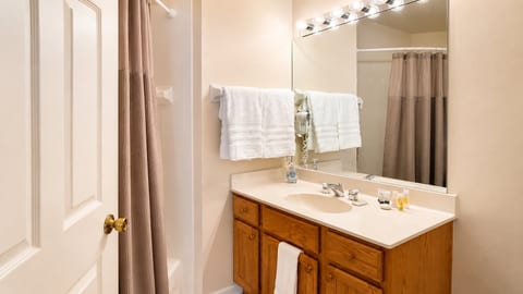 Clean bathroom with vanity storage, tile flooring, bright mirror lighting, and a tub/shower combination.