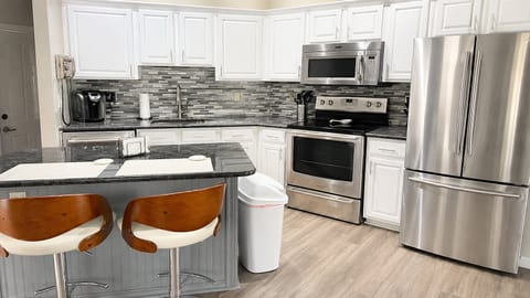 Modern kitchen with white cabinetry, stainless steel appliances, tile backsplash, breakfast bar seating, and wood-look flooring.