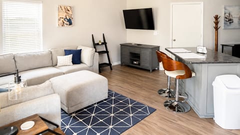 Comfortable living area with cozy sectional seating, wall-mounted TV, breakfast bar seating, and a bright open layout.