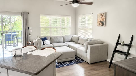 Spacious living area with large windows, comfortable sectional seating, and direct access to the private balcony.