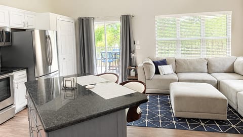 Updated open-concept kitchen and living area with stainless steel appliances, comfortable seating, and natural light from the balcony doors.