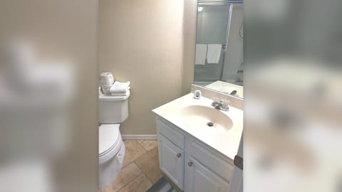 Bathroom with vanity storage, toilet, tile flooring, and bright mirror lighting.