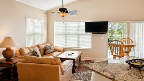 Spacious living area with comfortable seating, wall-mounted TV, dining space, and natural light from the balcony doors.