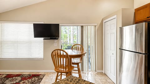 Dining area with a round table, wall-mounted TV, balcony access, and easy flow into the kitchen