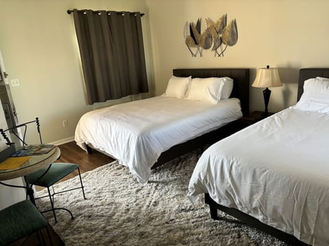 Bright bedroom featuring two beds, bedside lighting, and a small table with seating.