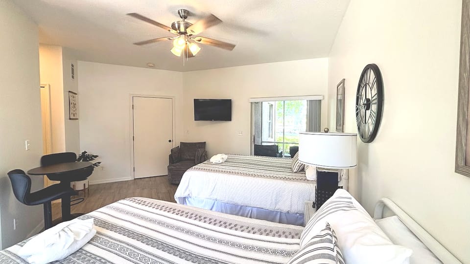 Spacious bedroom featuring two comfortable beds, ceiling fan, TV, and a bright, relaxing layout.