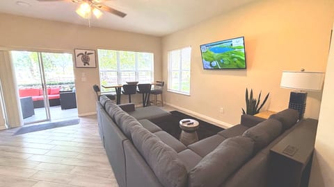 Bright open-concept living, dining, and kitchen area with comfortable sectional seating, tile flooring, and access to the patio.
