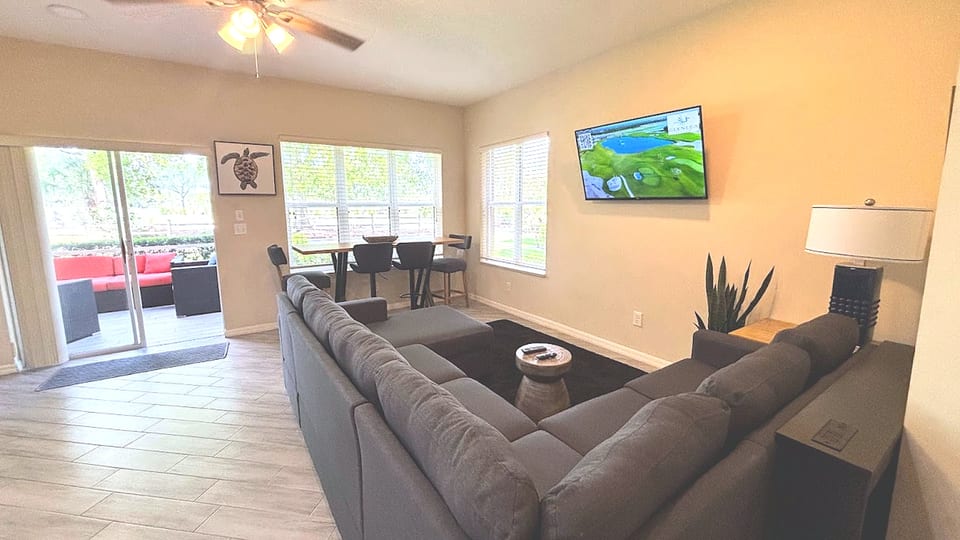 Bright open-concept living, dining, and kitchen area with comfortable sectional seating, tile flooring, and access to the patio.