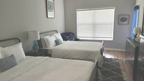 Comfortable bedroom with two beds, dresser storage, natural light, and soft neutral finishes.