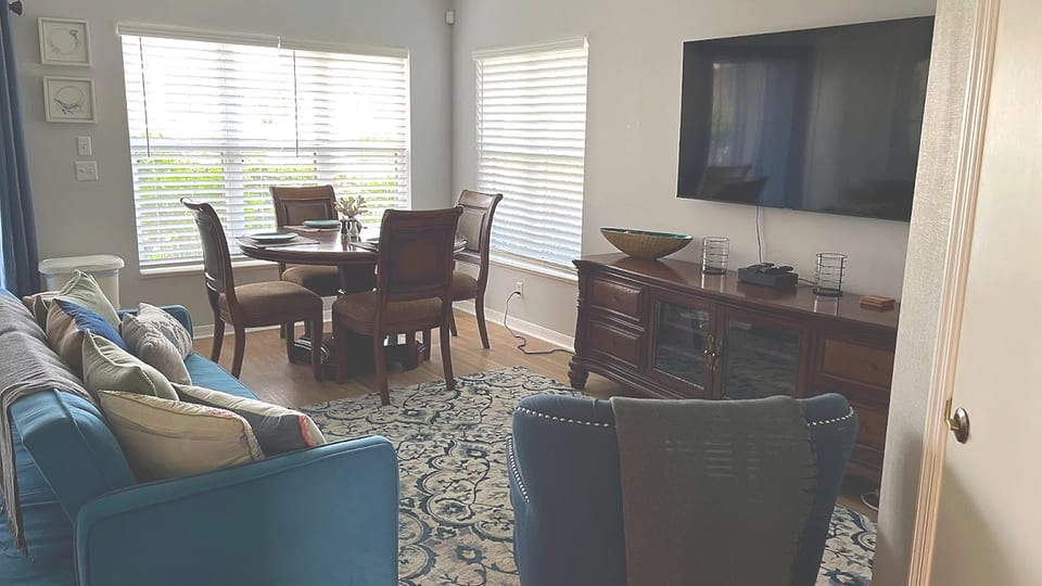 Comfortable living and dining area with blue accent seating, large windows, TV, and a bright open layout.