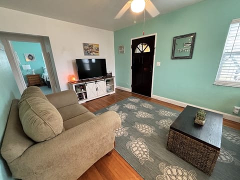 Bright living room with comfortable seating, TV, wood flooring, and a relaxed coastal atmosphere.