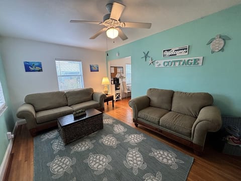 Comfortable living area with coastal decor, cozy seating, ceiling fan, and a welcoming cottage-style layout.
