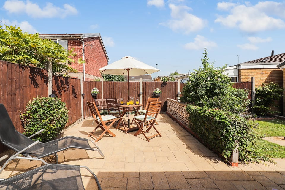 Sunny private patio sun trap with outdoor dining, parasol shade, loungers, and enclosed garden space
