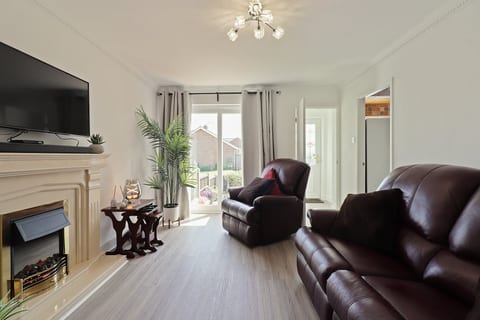 Bright lounge with leather seating, electric fireplace, Smart TV, soundbar, and patio doors to the garden