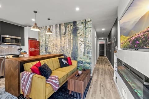 Relax in this living room with a cozy couch and serene forest mural. Perfect for unwinding or hosting, this space offers comfort with artistic flair. The hallway leads to more thoughtfully designed rooms, ensuring a memorable stay for all guests.