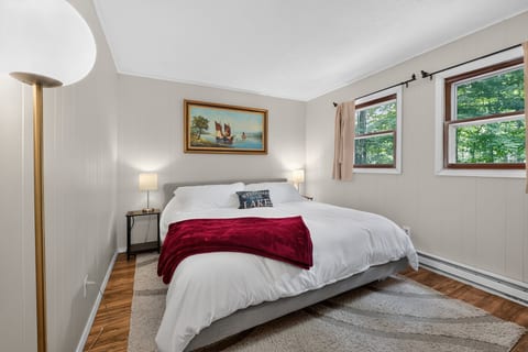 Bright, cozy bedroom with queen bed, soft lighting, and peaceful wooded views