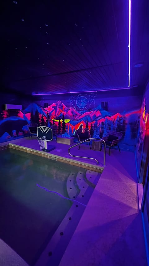 Neon-lit indoor pool with mural, lounge seating, and poolside hoop